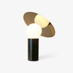 Clérachic disc table lamp on a plain white background, its dark marble base topped by a gold-toned panel over the glass globe.
