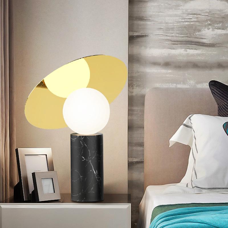 Clérachic disc lamp lit on a bedside cabinet holding two framed photos, beside a dusty pink headboard and a teal throw.