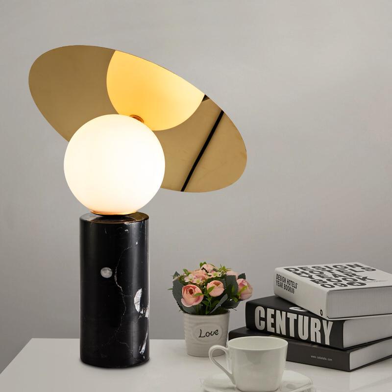 Styled with a small planter, coffee cup and saucer, the Clérachic disc lamp glows on a white side table beside a stack of books.
