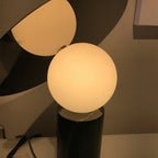 Extreme close-up of the Clérachic lamp's gold-toned panel and lit frosted glass globe, a dim interior blurred behind it.