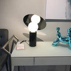Tufted grey chairs frame the scene as the Clérachic disc lamp glows on a showroom desk beside a chrome balloon-dog ornament.