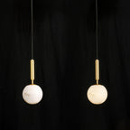 Close-up against black of the brushed brass stem meeting the top of the alabaster globe.