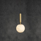 Alabaster globe pendant on a brass stem, hung on a black cord against a dark grey wall.