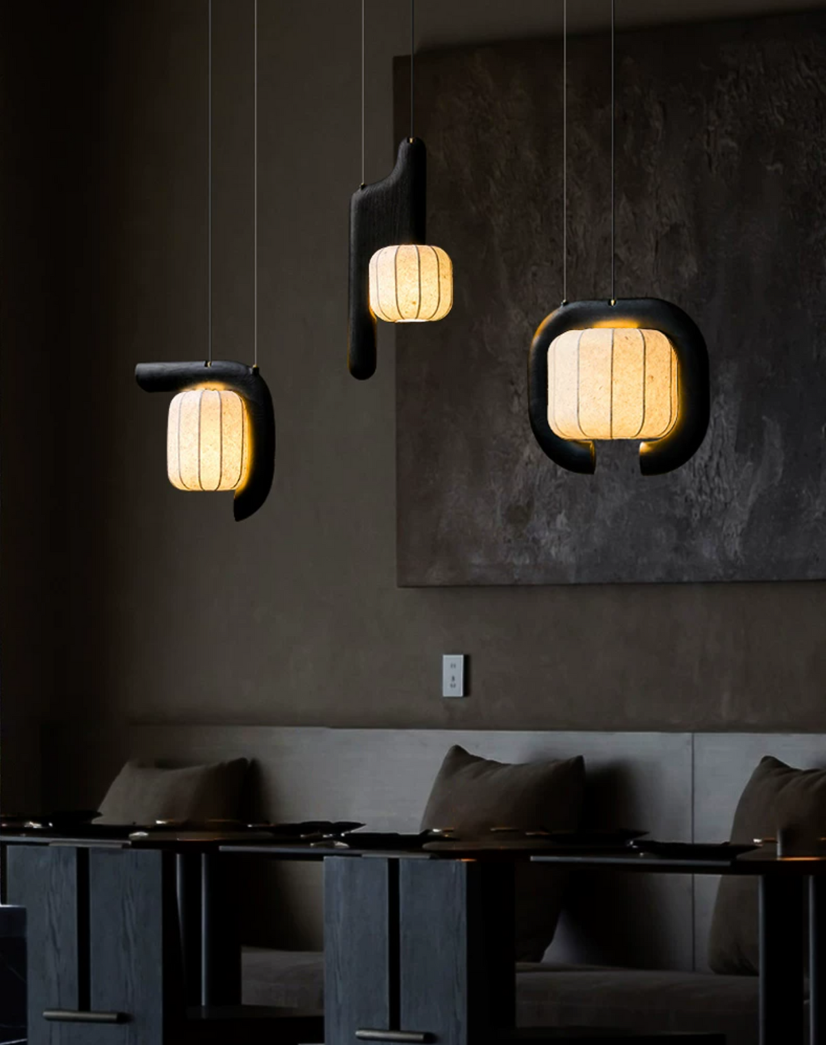 Against a dark wall hung with art, three shades of this black Clérachic fixture glow above bench seating.