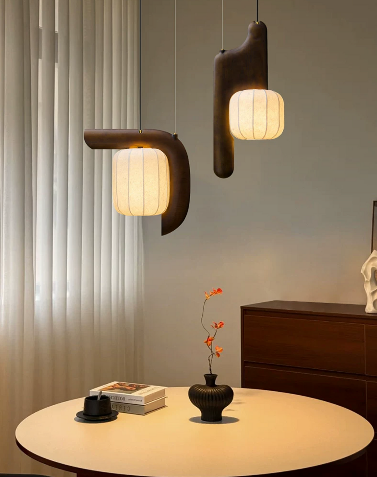 Two shades of this dark wood Clérachic fixture glow above a small table set with books and a vase, curtains behind.