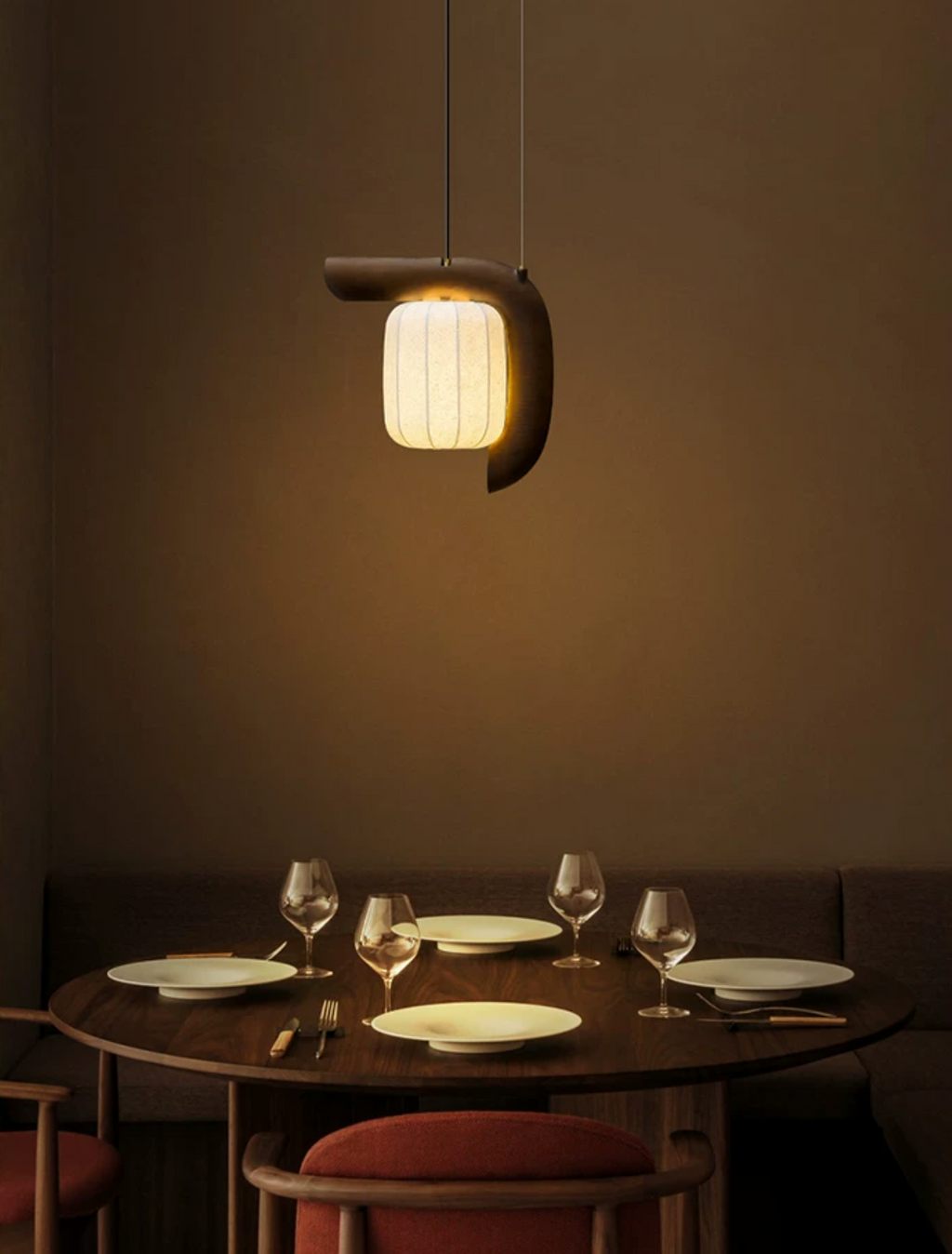This dark wood, bent-style Clérachic pendant glows above a round table set with wine glasses and pink chairs.