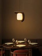 This dark wood, bent-style Clérachic pendant glows above a round table set with wine glasses and pink chairs.