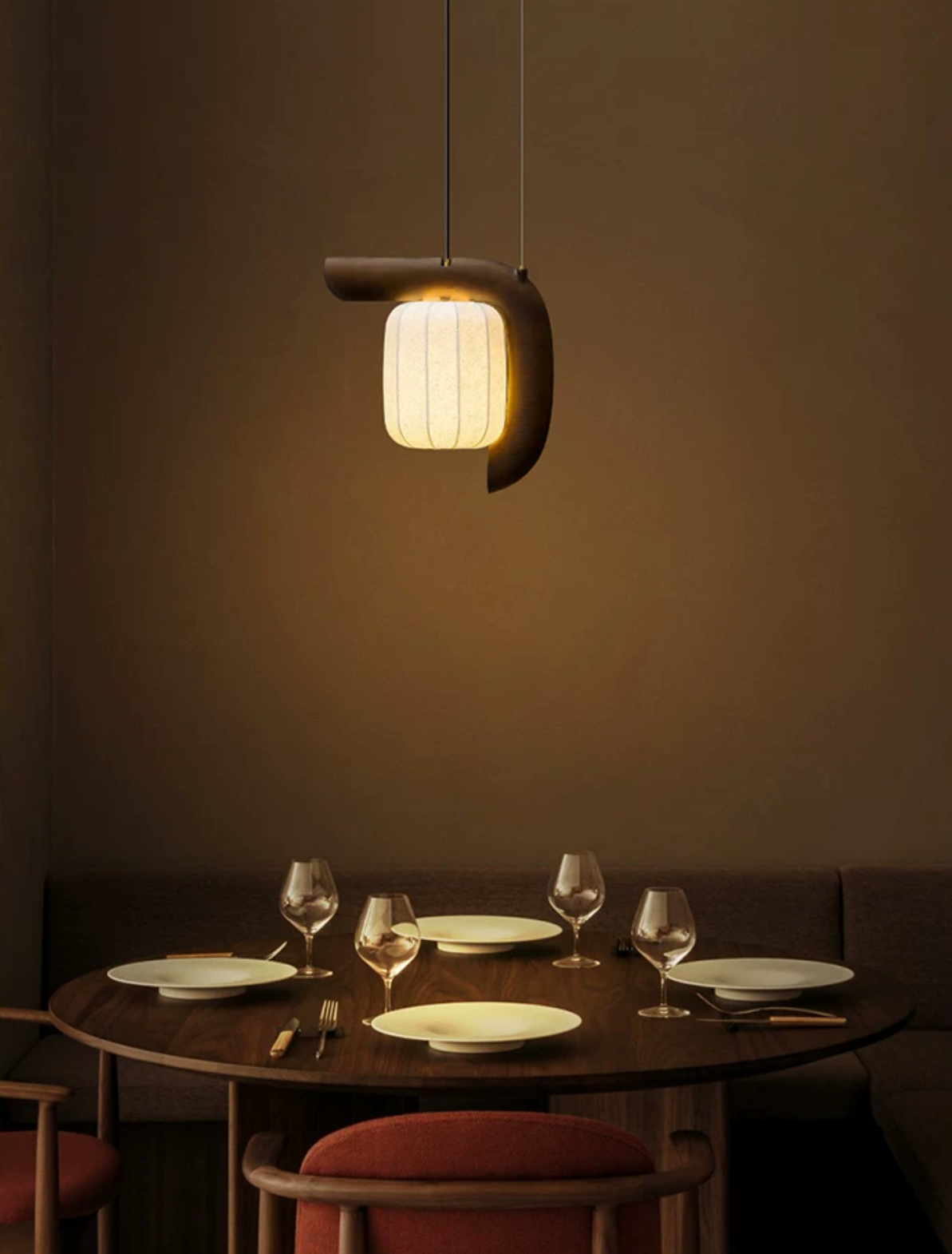 This dark wood, bent-style Clérachic pendant glows above a round table set with wine glasses and pink chairs.
