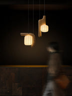 Before a textured stone wall, two shades of this dark wood Clérachic fixture glow as a figure passes below.