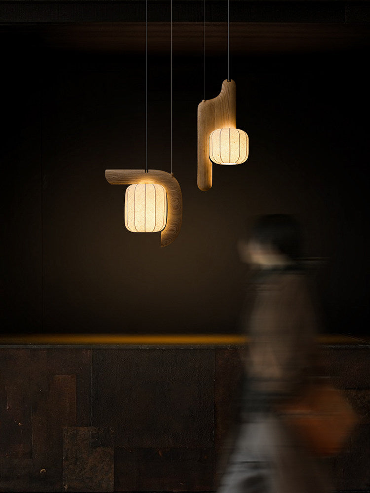 Before a textured stone wall, two shades of this dark wood Clérachic fixture glow as a figure passes below.