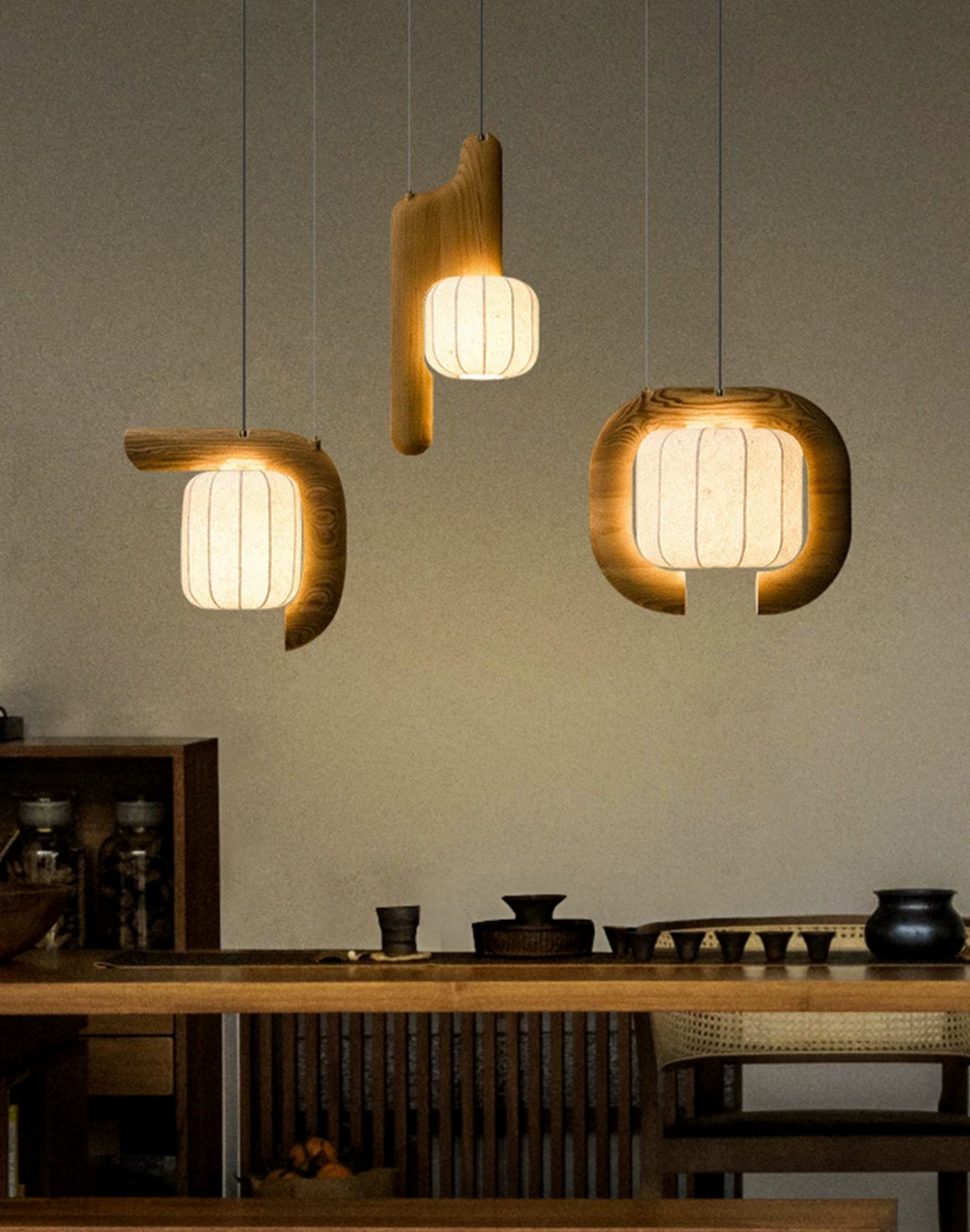 Above a wood counter set with small teacups, three shades of this dark wood Clérachic fixture glow warm.