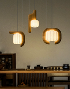 Above a wood counter set with small teacups, three shades of this dark wood Clérachic fixture glow warm.