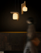 Two shades of this dark wood Clérachic fixture glow above a dark counter as someone walks past below.