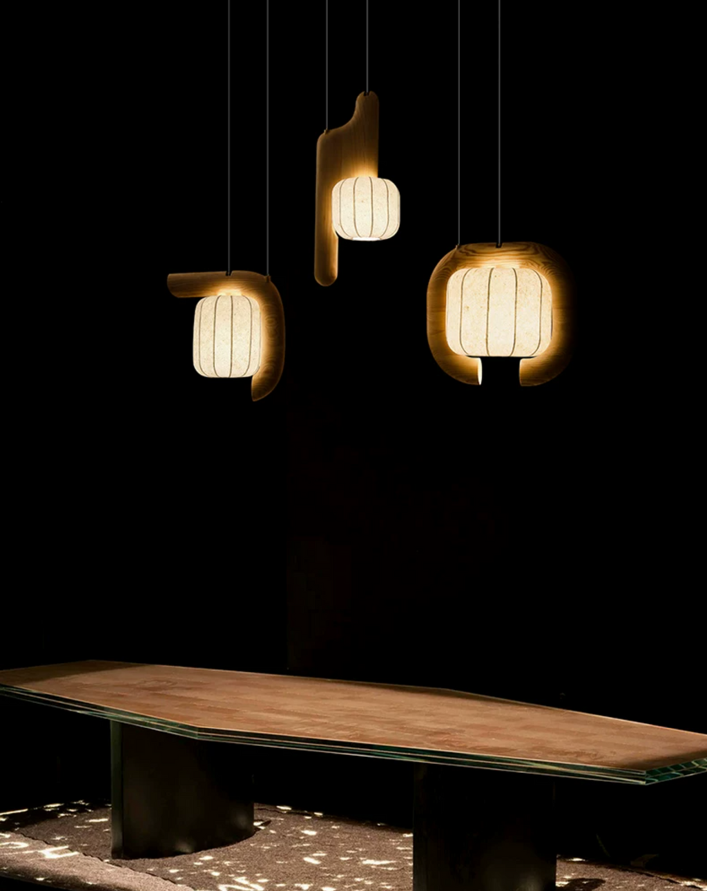 In a very dim room, three shades of this dark-finished Clérachic fixture cast warm light onto a pale wood bench below.