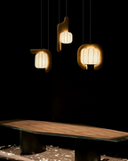 In a very dim room, three shades of this dark-finished Clérachic fixture cast warm light onto a pale wood bench below.