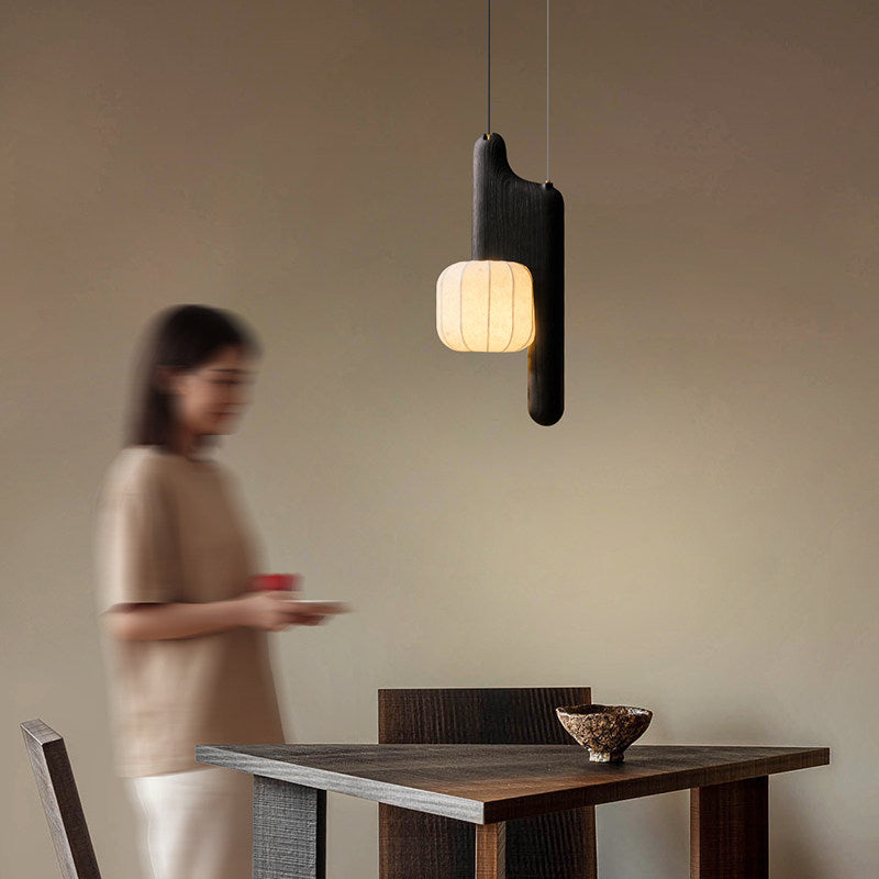This black, vertical-style Clérachic pendant glows in a plain room as a figure walks past in the background.