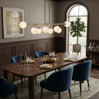 This brushed-brass Clérachic chandelier lights a dining table beneath an arched window and a fiddle-leaf fig.