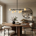The matte-black Clérachic chandelier glows above a round table near a large round mirror.