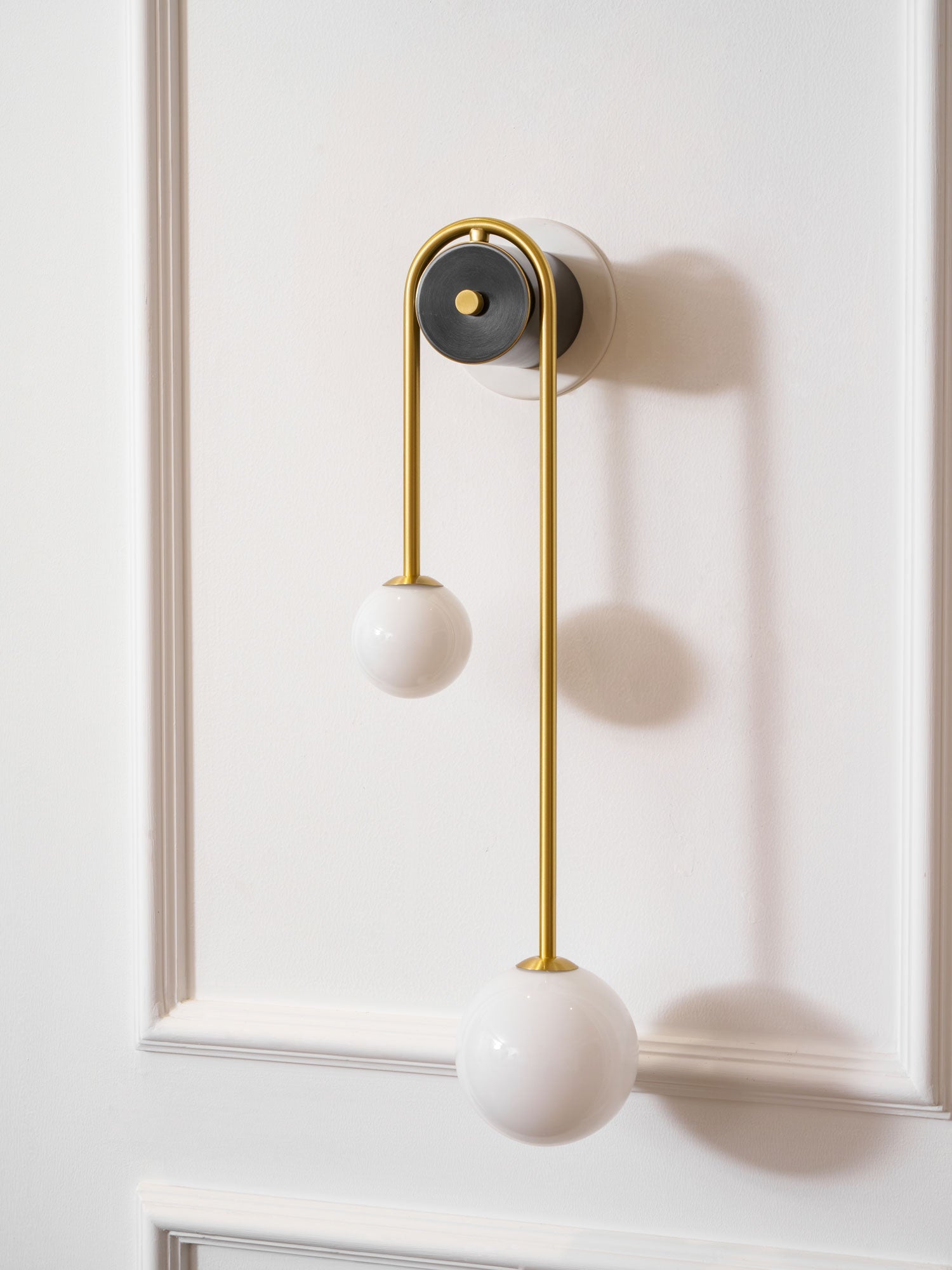 Curved brass wall light glowing warmly with two glass shades