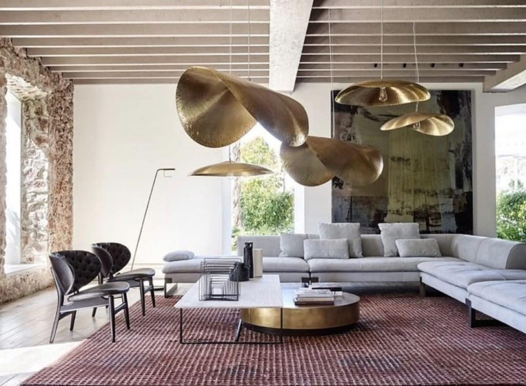 Clérachic hammered brass shades hang in a rustic living room with stone walls and a grey sofa.