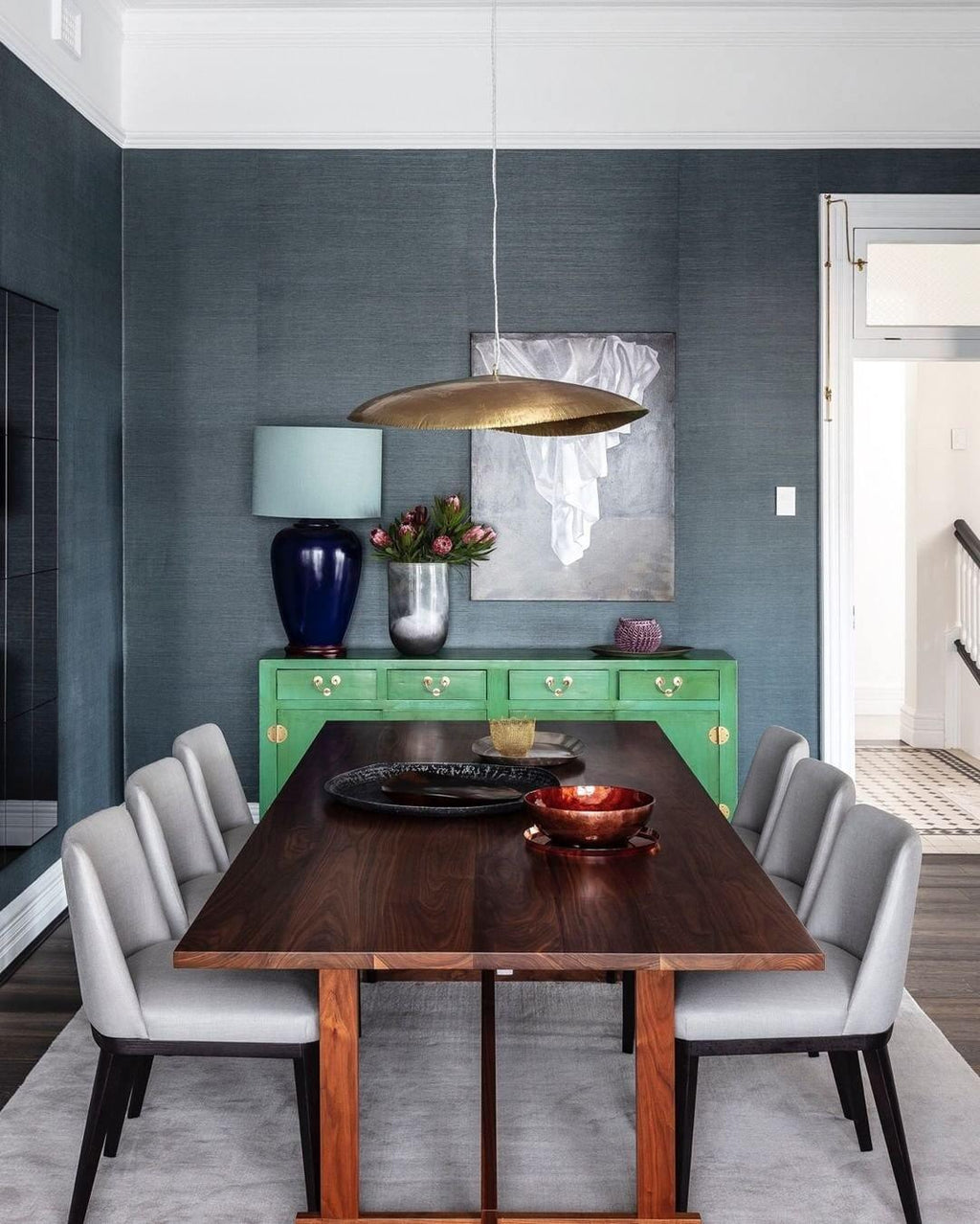 A single lit Clérachic pendant hangs above a wood table in a dining room with teal walls.