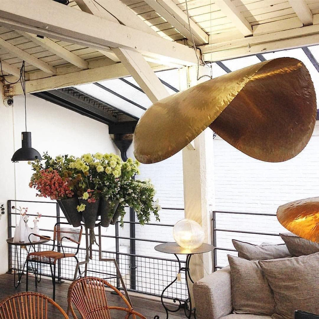 This Clérachic hammered brass shade hangs unlit on an open patio beneath a wood beam ceiling.