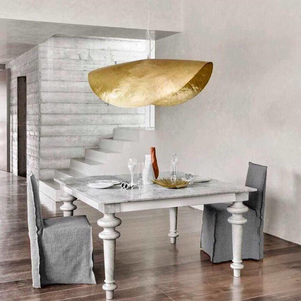 This Clérachic hammered brass shade hangs unlit at the top of a staircase near a dining table.