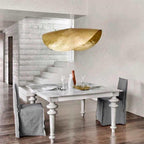 This Clérachic hammered brass shade hangs unlit at the top of a staircase near a dining table.