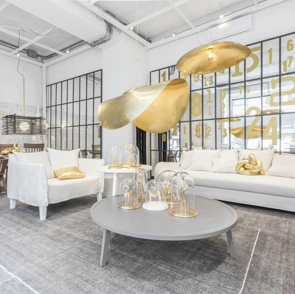 Two lit Clérachic pendants hang in a white showroom with a glass partition and a sofa.