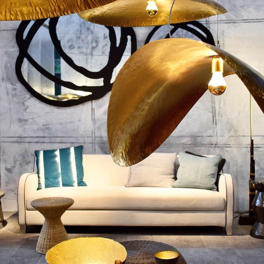Lit gold, this Clérachic pendant hangs in an industrial loft beside a round mirror sculpture.