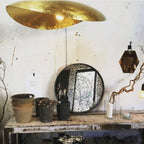 Seen from below, this Clérachic hammered brass shade glows above a table set with pots and mirrors.