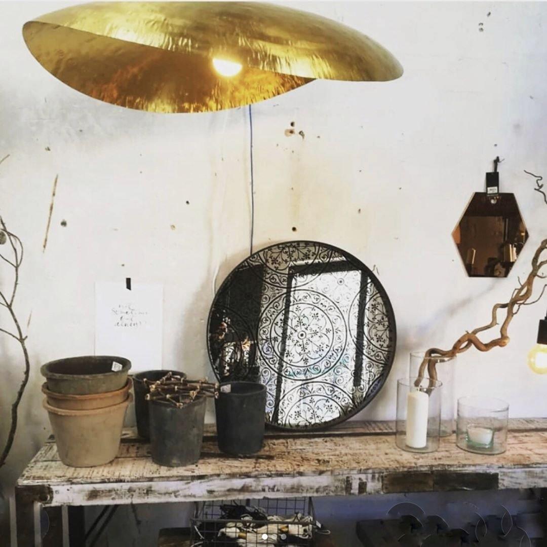 Seen from below, this Clérachic hammered brass shade glows above a table set with pots and mirrors.