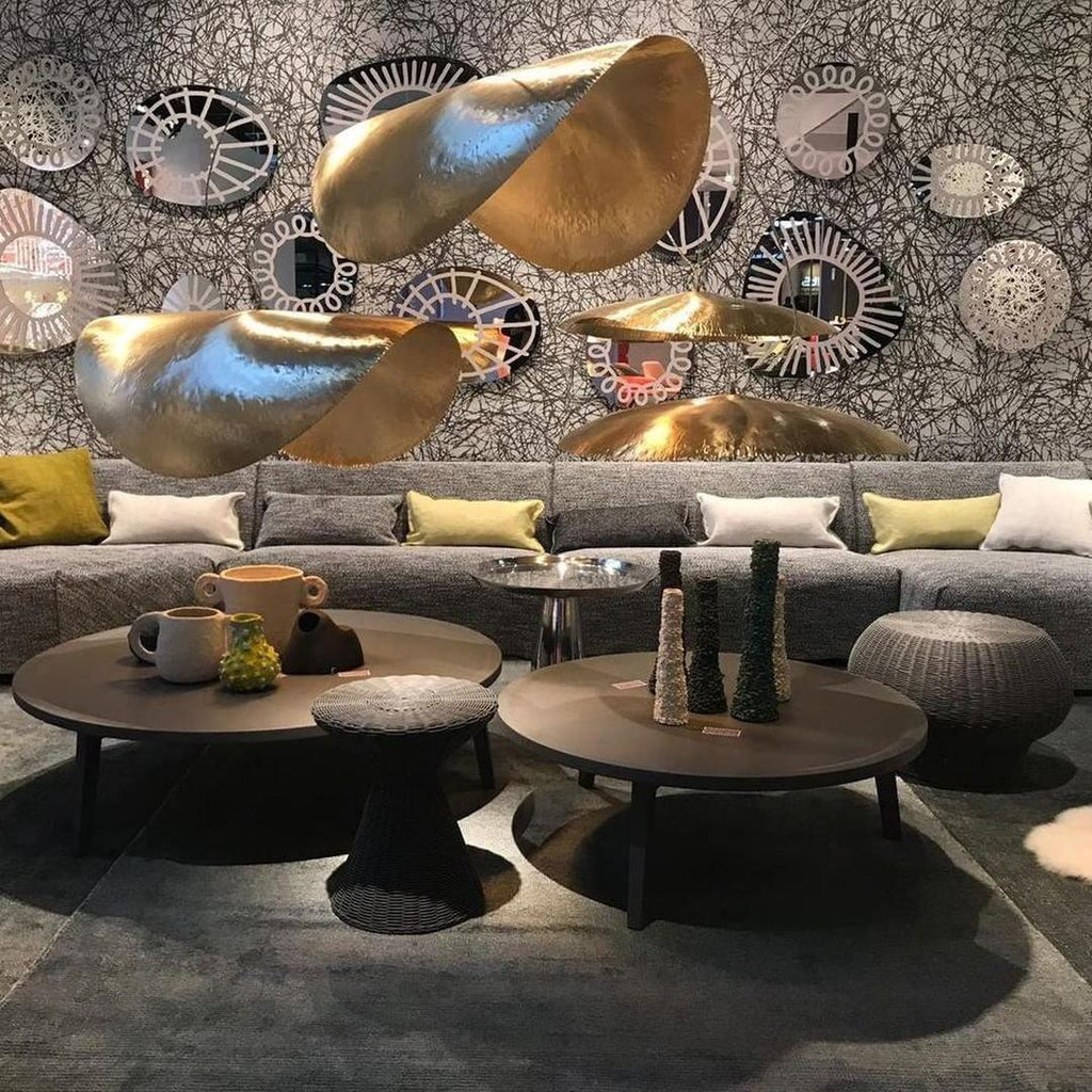 Hammered brass shades from Clérachic hang before a wall of decorative plates above a grey sofa.