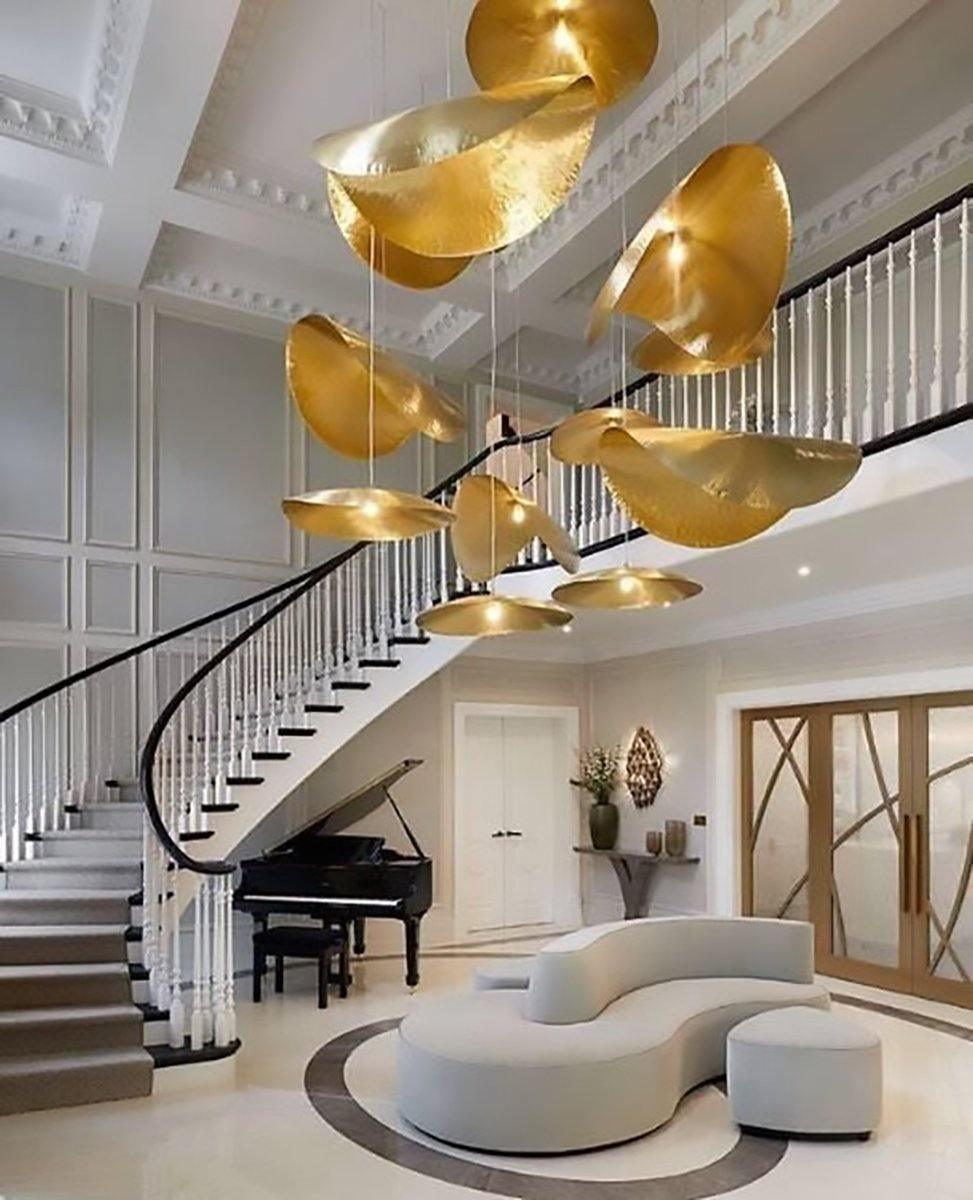 A cluster of Clérachic hammered brass shades hangs over a staircase beside a grand piano.
