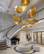 A cluster of Clérachic hammered brass shades hangs over a staircase beside a grand piano.