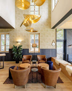 A cluster of Clérachic pendants hangs in a tall stairwell lined with patterned wallpaper.