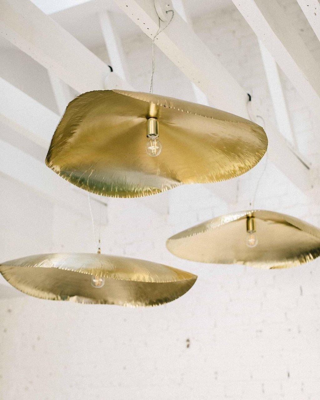 Three hammered brass shades from Clérachic are seen from below in a white beamed room.