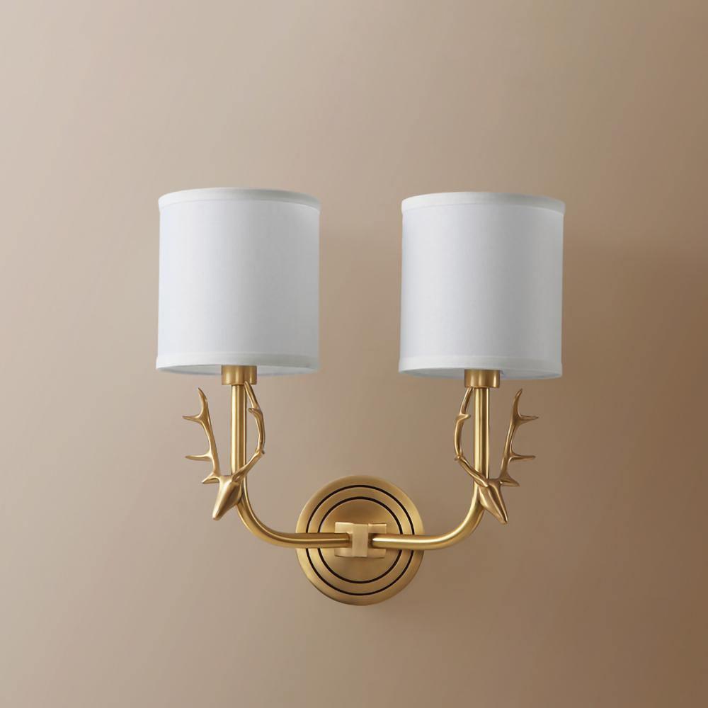 Brass deer head sconce with two white linen shades in a room