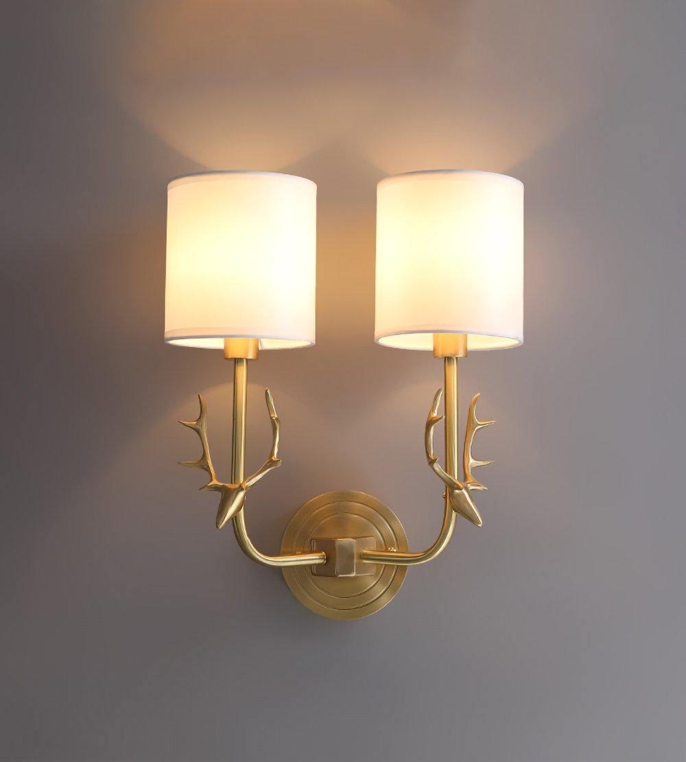 Brass deer head wall light glowing softly with white linen diffusers