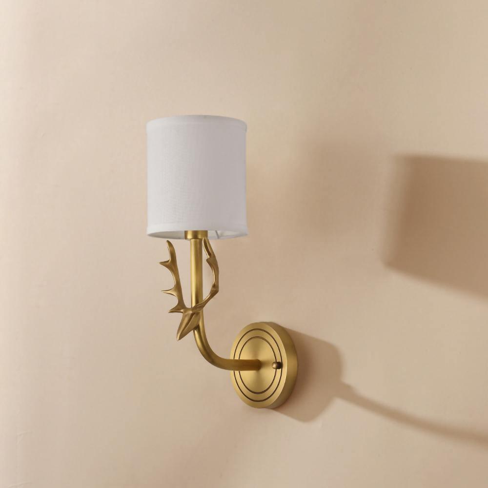 Brass antlered wall light glowing through two soft linen shades