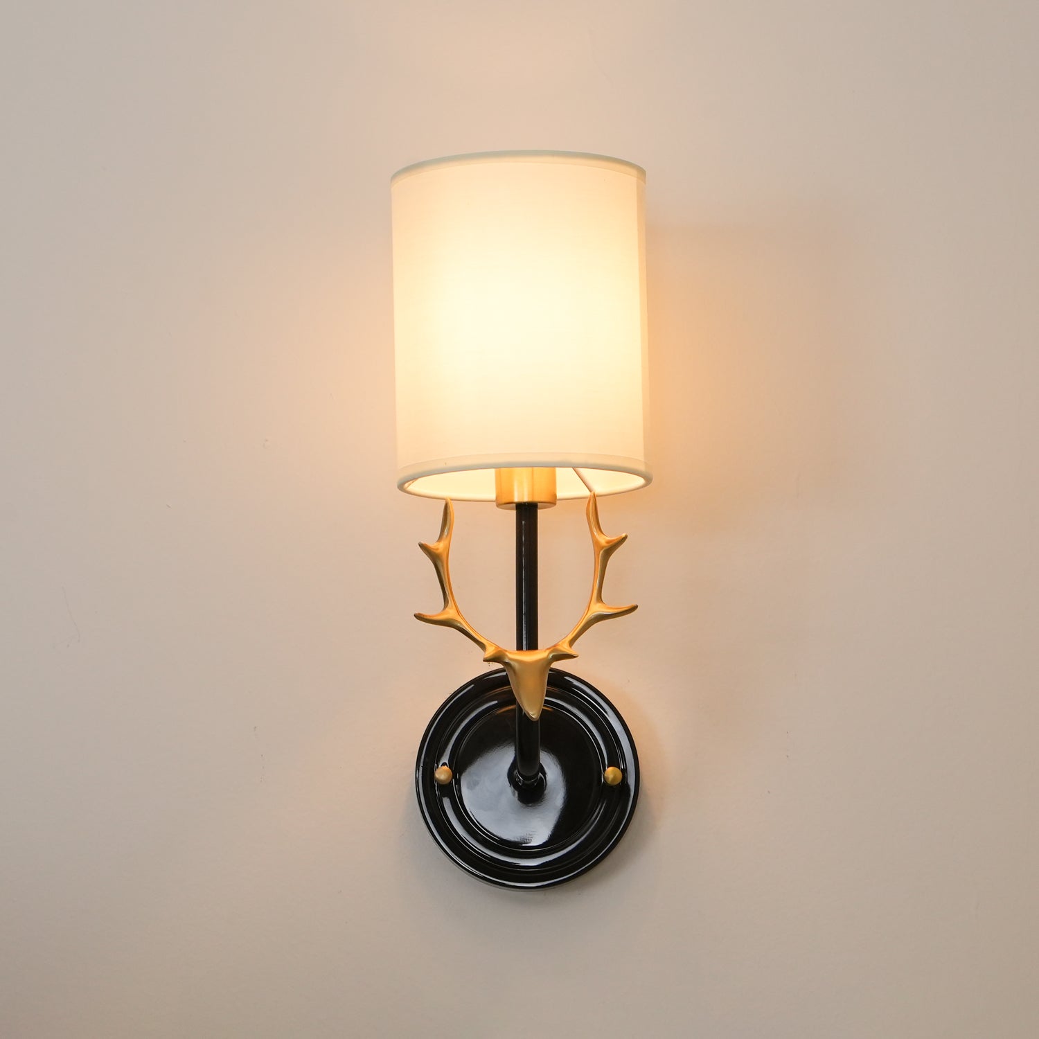 Brass antler wall light with two warm glowing linen lampshades