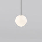 Opal glass globe pendant glowing warmly on a brass rod