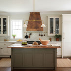 This Clérachic pendant glows warm above a sage-green kitchen island set with bowls of fruit and bread.