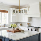 Navy cabinetry frames this Clérachic pendant, glowing warm above a marble island with a cutting board and flowers.