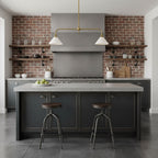 Exposed brick and open shelving frame this Clérachic pendant, glowing warm above a dark island with bar stools.