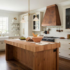 This Clérachic pendant glows warm above a butcher-block island set with bread, a copper range hood overhead.