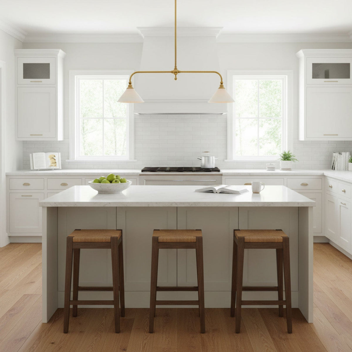 Grey cabinetry and wood stools sit beneath this Clérachic pendant, glowing warm above a kitchen island near a window.