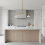 Pale wood cabinetry and a stone hood frame this Clérachic pendant, glowing warm above a minimalist kitchen island.