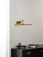 Slim gold wall light glowing above a framed artwork display