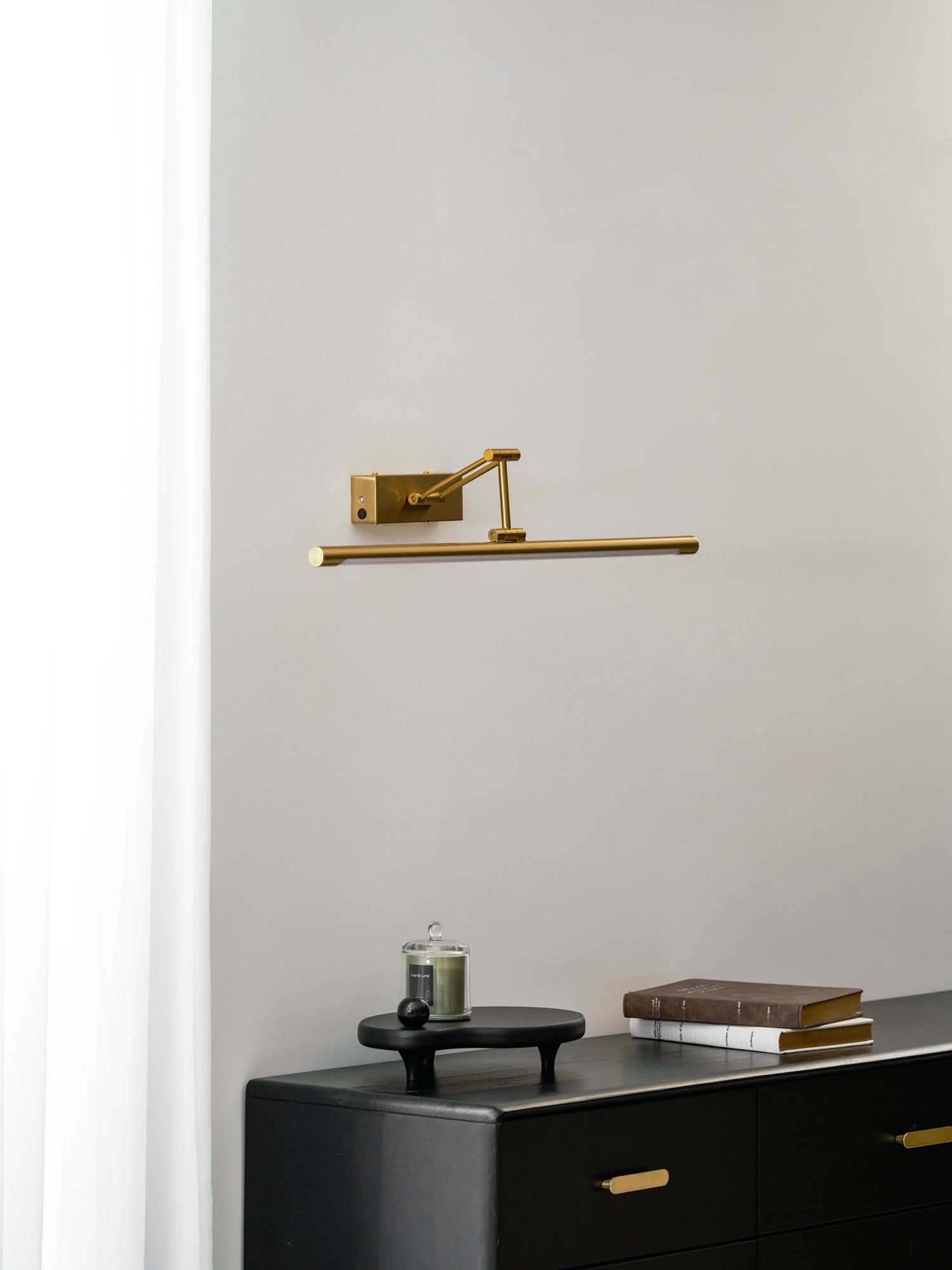 Slim gold wall light glowing above a framed artwork display